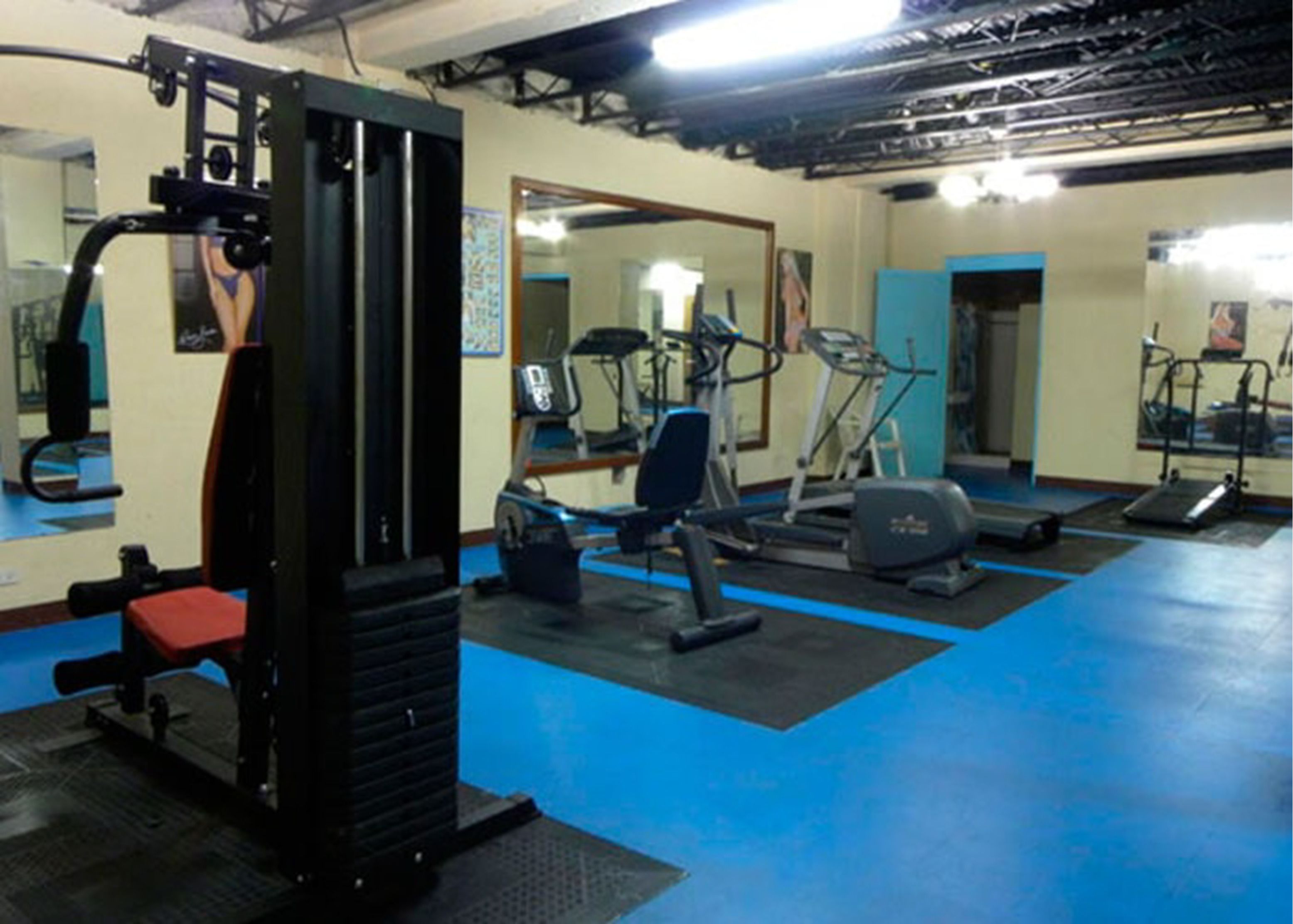 A gym with exercise equipment, a mirror, and a blue floor.