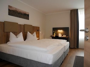 A hotel room with a large bed, a desk with a lamp, and a painting on the wall.