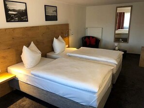 A hotel room with two beds, a wooden headboard, a nightstand, a chair, a mirror, and framed pictures on the wall.