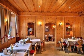 A wooden-paneled dining area with tables set for meals, featuring wall-mounted lamps and a framed picture.