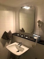 Un baño con un lavamanos blanco, un espejo, un toallero y un secador de pelo.
