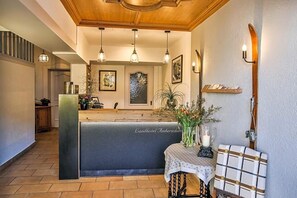 A reception area with a wooden reception desk, pendant lighting, framed artwork on the wall, and a small table with a vase of flowers.
