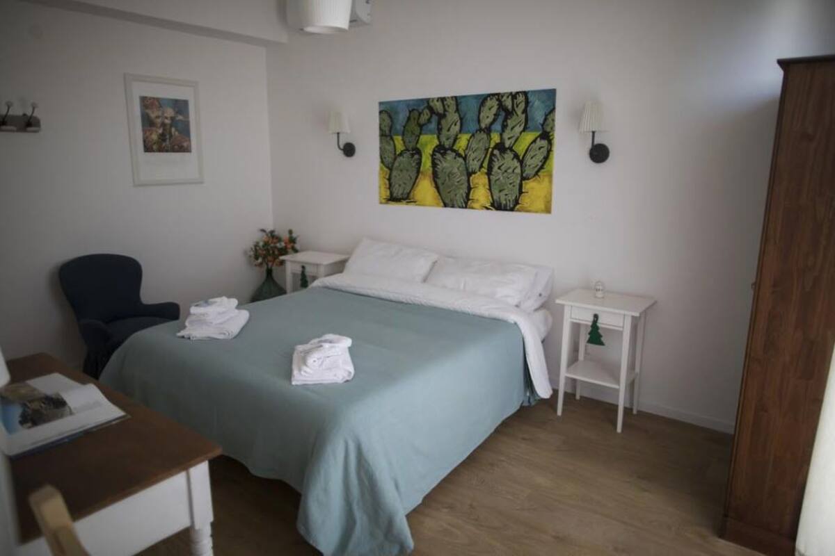 A hotel room with a bed, a chair, a small table, and a nightstand with a lamp.