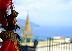 A person in traditional attire with a blurred background of a building and a fence. - B&B Tauromenion (Taormina)