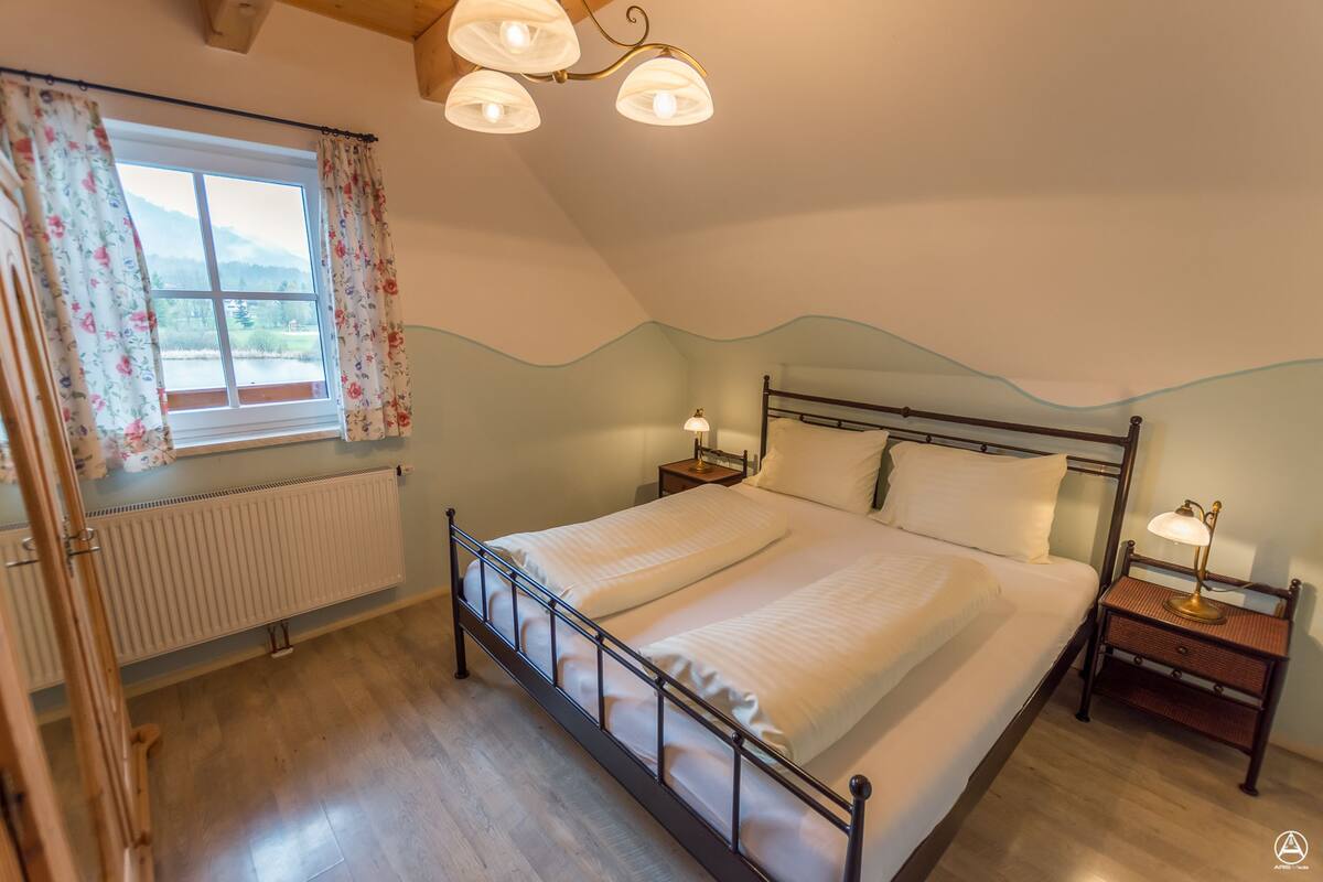 A bedroom with a bed, two bedside tables, a window with curtains, and a radiator.