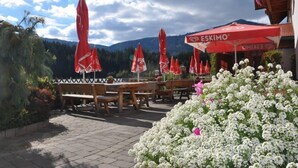 An outdoor seating area with wooden tables and benches, red umbrellas, and white flowers. - Gasthof Fischerwirt (Neumarkt in Steiermark)