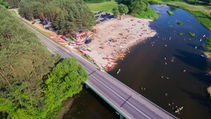 An aerial view of a riverside beach with boats, a parking area, and a bridge. - Domki Wiosełko (Nasielsk)