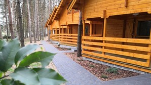 A row of wooden cabins with a paved walkway in between. - Domki Wiosełko (Nasielsk)