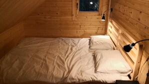 A small, cozy wooden cabin room with a single bed, a window, and a desk lamp. - Domki Wiosełko (Nasielsk)