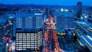 A modern cityscape at dusk with illuminated buildings, a busy intersection, and a prominent hotel with a sign. - Daiwa Roynet Hotel Hiroshima Station (Hiroshima)