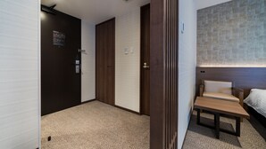 Una habitación de hotel con cama, una mesita, una silla y un televisor montado en la pared.