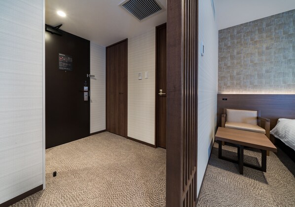 Una habitación de hotel con cama, una mesita, una silla y un televisor montado en la pared.