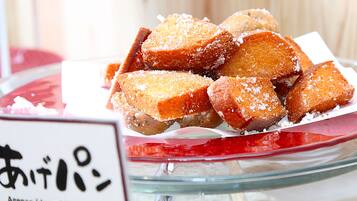 A glass bowl filled with deep-fried bread pieces, dusted with sugar, on a table with a sign in a foreign language.