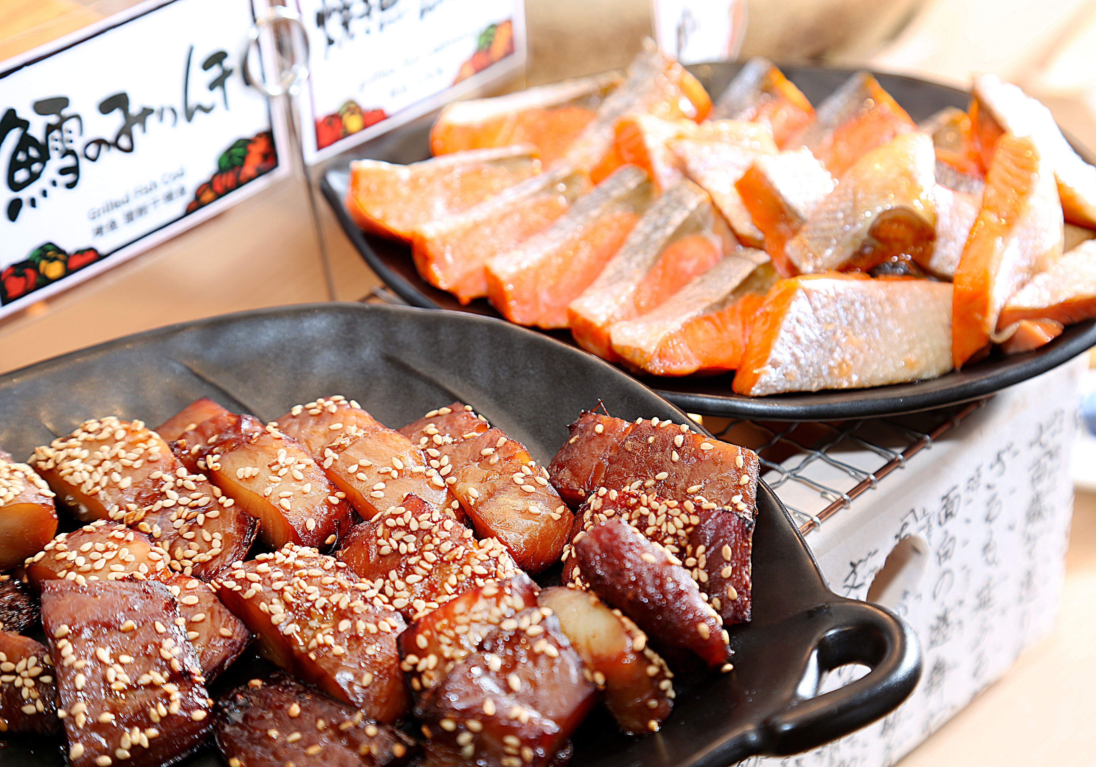 A variety of cooked meats, including pork belly and salmon, garnished with sesame seeds.