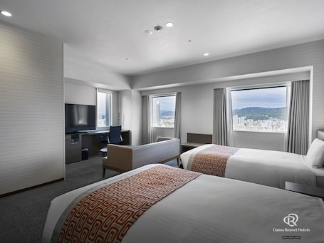 A hotel room with two beds, a desk, a TV, and large windows offering a city view.