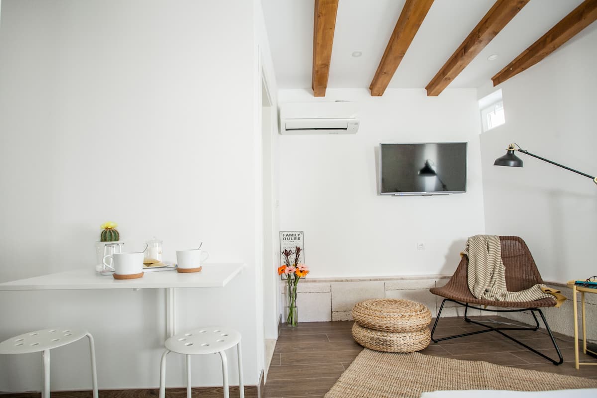 A modern living room with a white table, two white chairs, a TV mounted on the wall, a wooden ceiling, a TV stand, and a chair with a blanket.