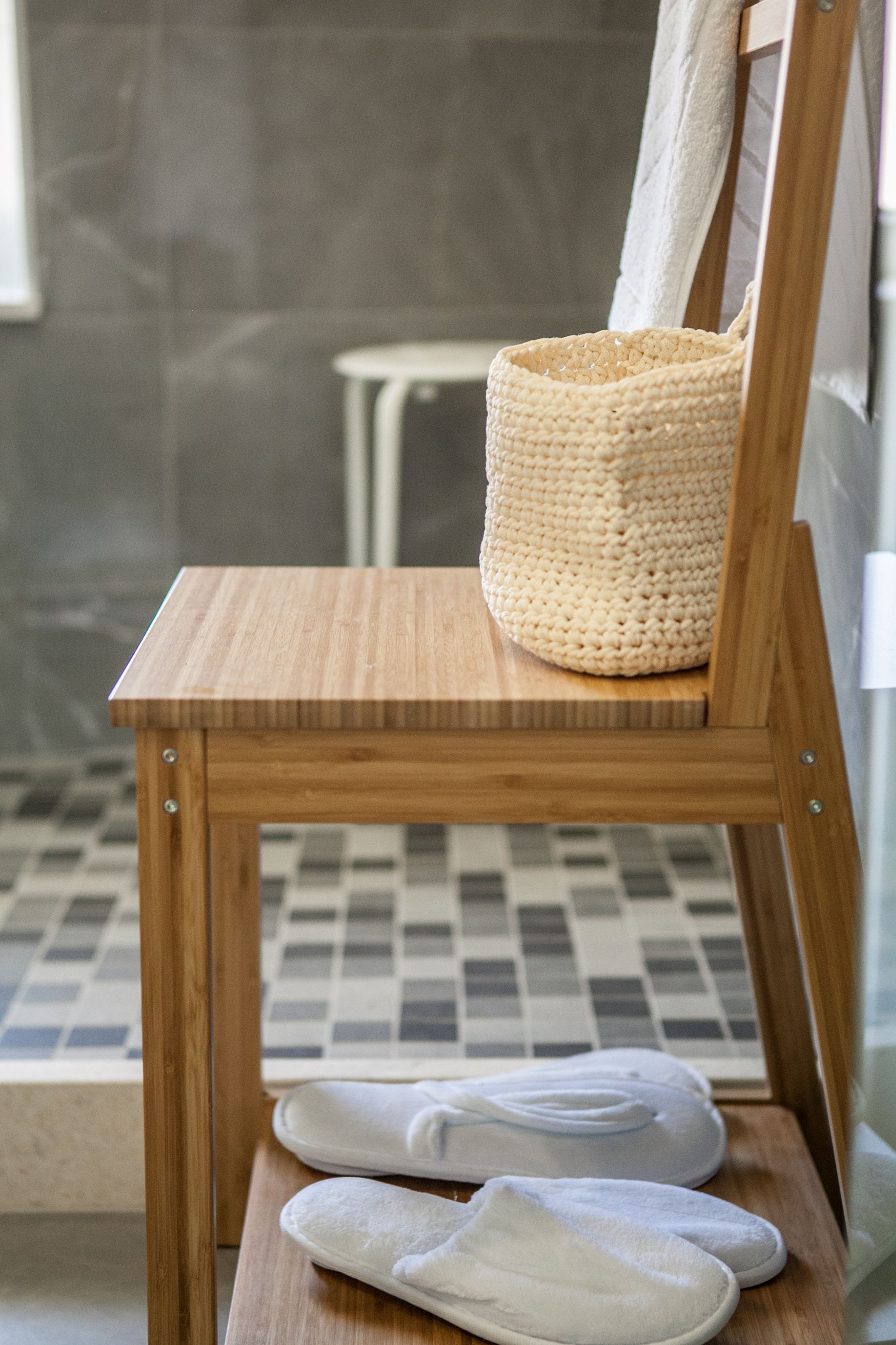 Una silla de madera con una cesta tejida y zapatillas blancas sobre un suelo de baldosas.