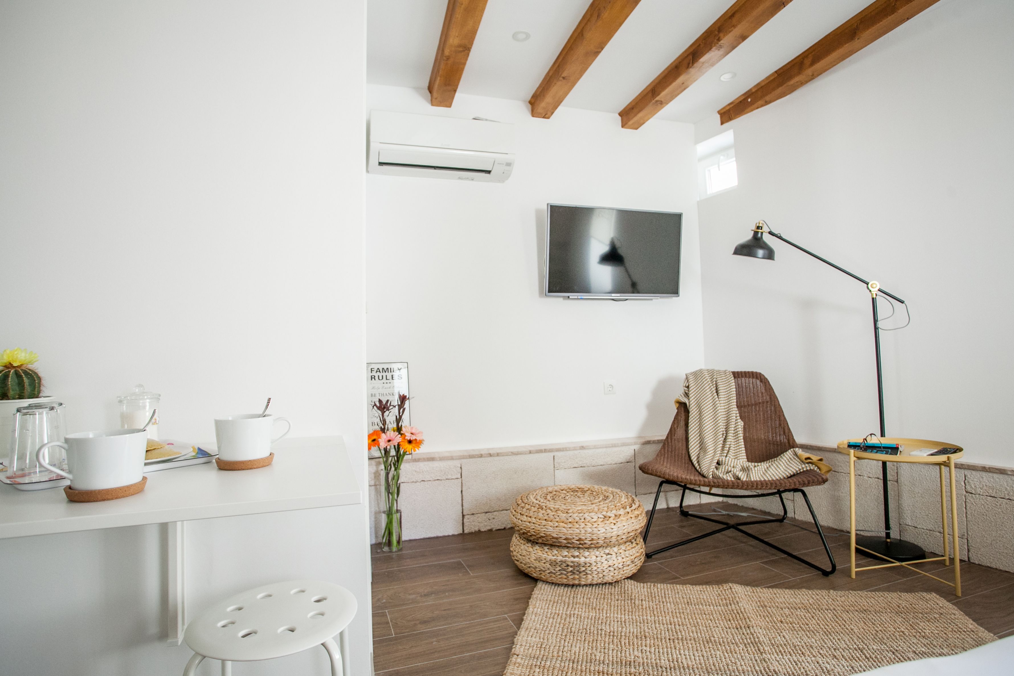 Uma sala de estar moderna com uma televisão de tela plana, teto de madeira, uma poltrona confortável, uma pequena mesa lateral e uma mesa de centro.
