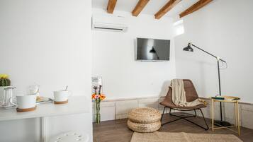 Uma sala de estar moderna com uma televisão de tela plana, teto de madeira, uma poltrona confortável, uma pequena mesa lateral e uma mesa de centro.