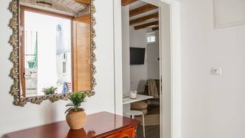 Un aparador de madera con espejo, una planta en maceta y un tapete de bienvenida en una habitación con paredes blancas y vigas de madera.