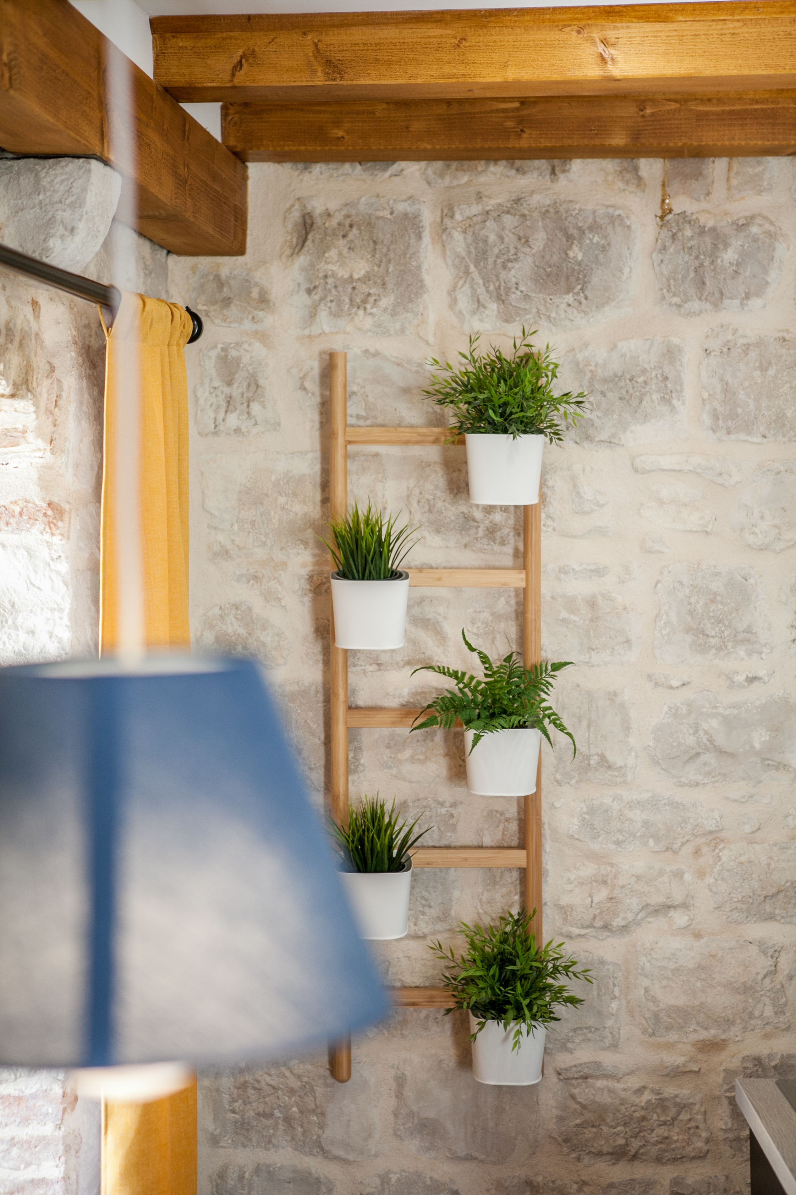 A wooden ladder shelf with potted plants against a stone wall.