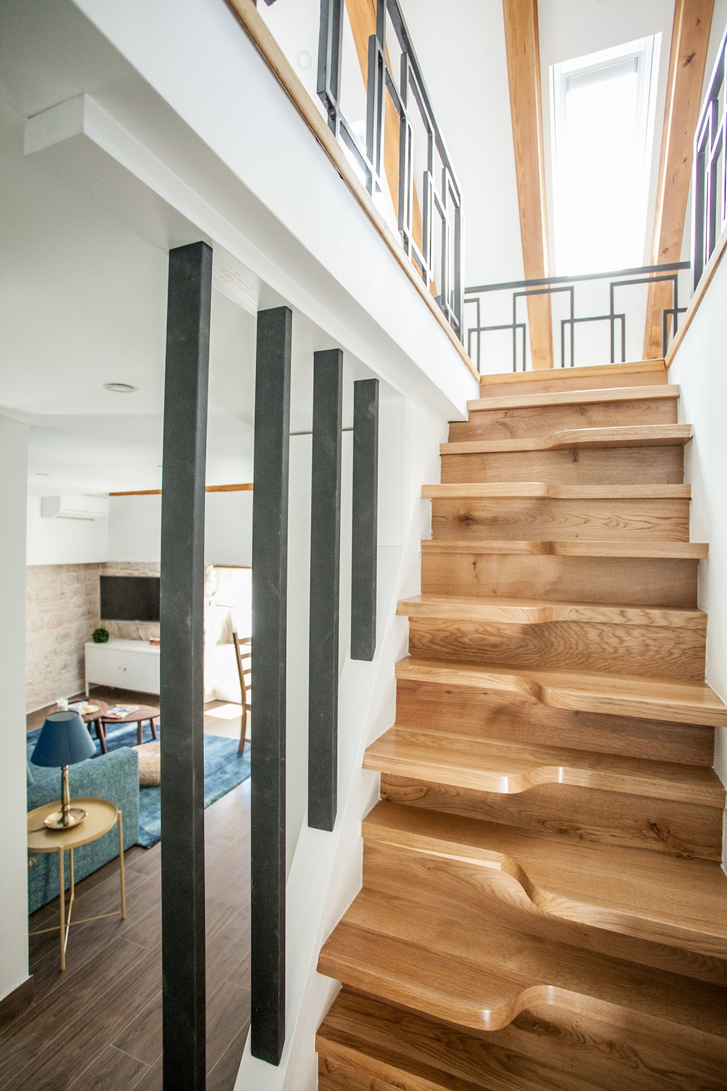 Un escalier en bois au design moderne, menant à un espace situé au deuxième étage et offrant une vue sur l’extérieur.