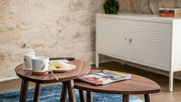 A small round wooden table with a magazine, a glass of milk, a plate with a pastry, and a remote control.