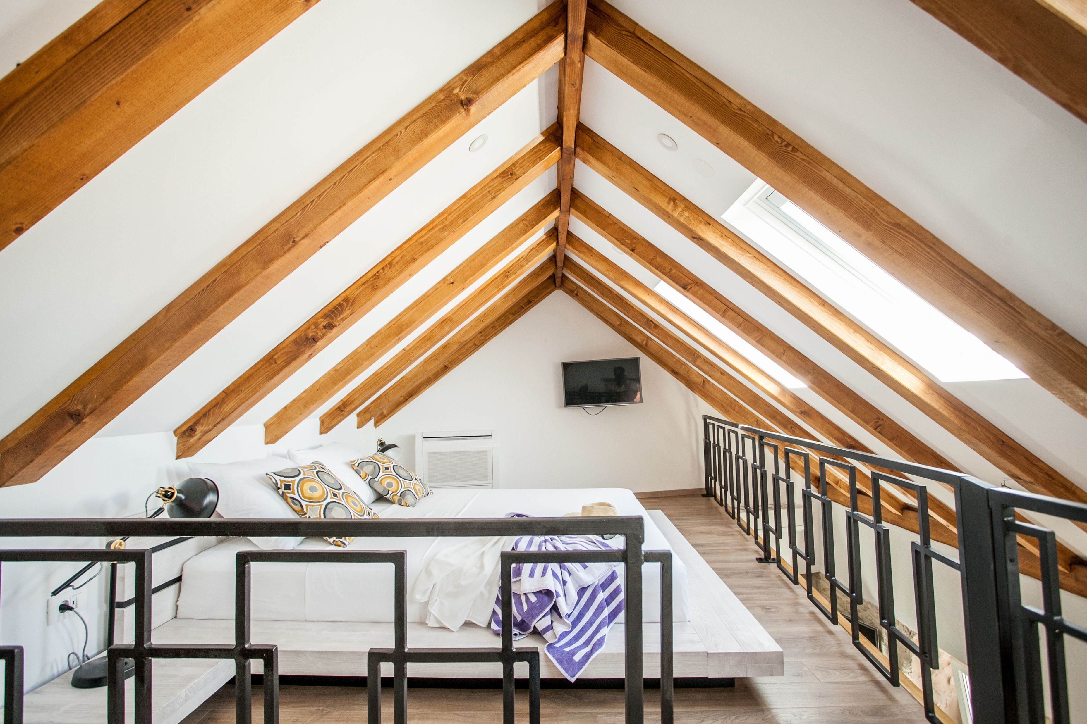 A bedroom with a sloped ceiling, a bed, a TV, and a wooden railing.