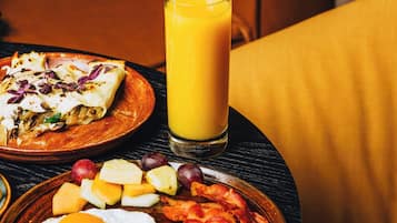 A breakfast setting with a plate of eggs, bacon, and fruit, a glass of orange juice, and a quesadilla on a table.