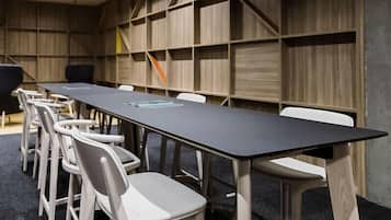 A conference room with a long table and white chairs, wooden panel walls, and a dark carpet.