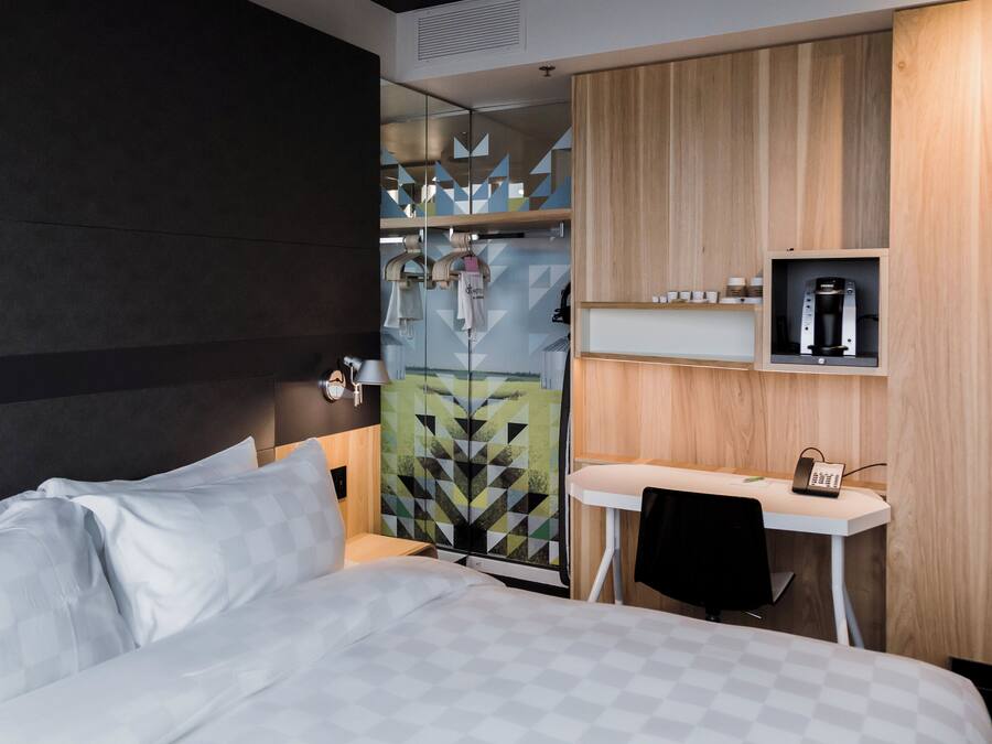 A hotel room with a bed, a desk, and a shower area.