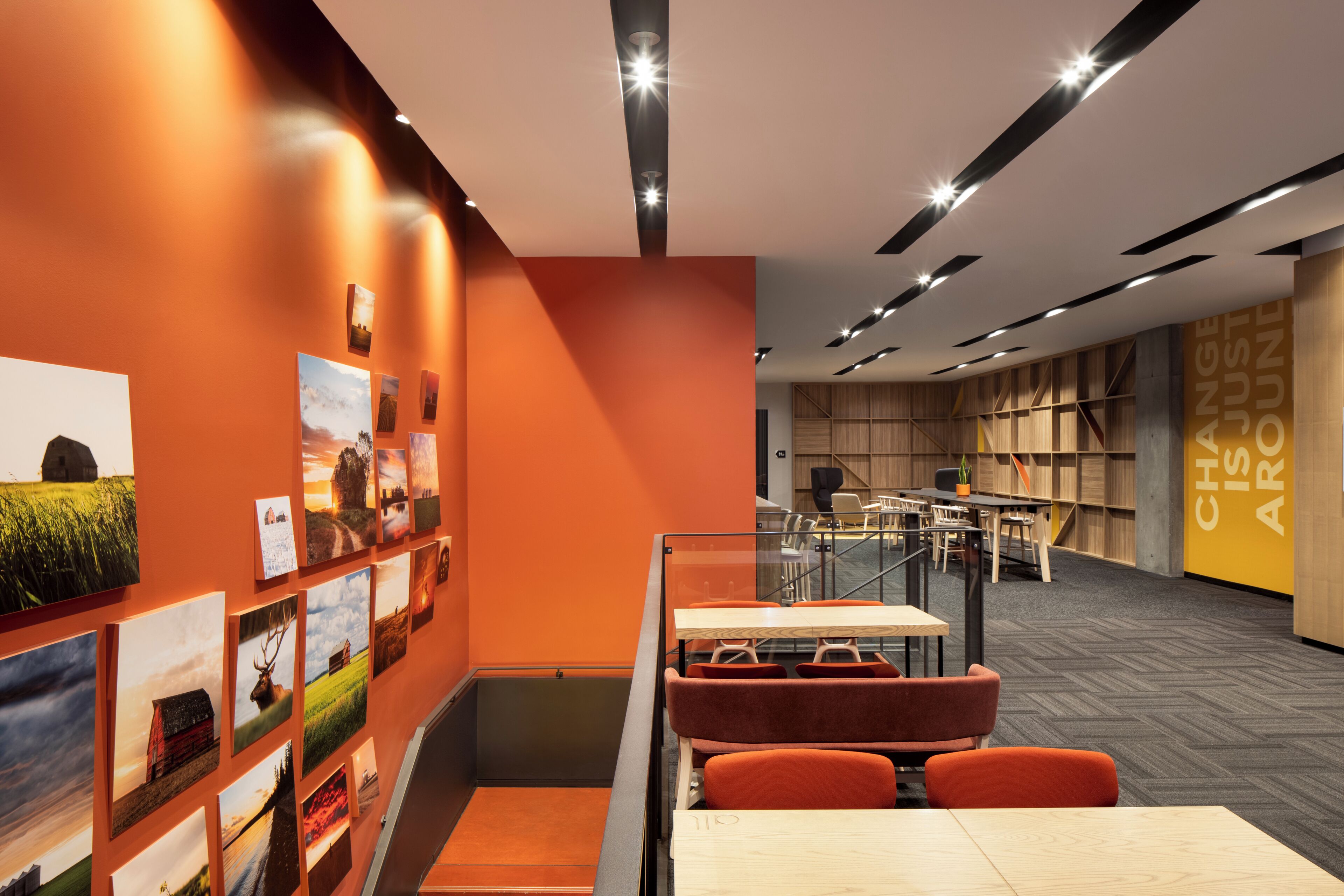 A modern library with orange walls, wooden bookshelves, and a seating area with orange chairs.