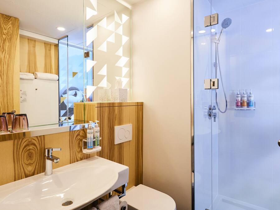 Un baño moderno con tocador de madera, cabina de ducha de vidrio y un espejo grande.