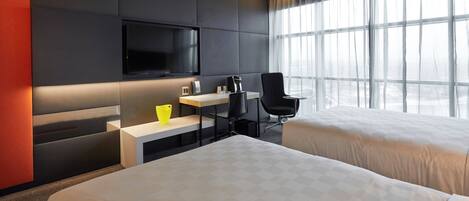 A modern hotel room with two beds, a desk with a coffee maker, a TV, and a large window with curtains.