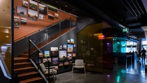 Un interior moderno con escalera, zona de estar y una pared de vidrio con obras de arte.