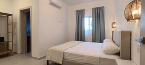 Un dormitorio con cama, armario, estante y ventana con cortinas.