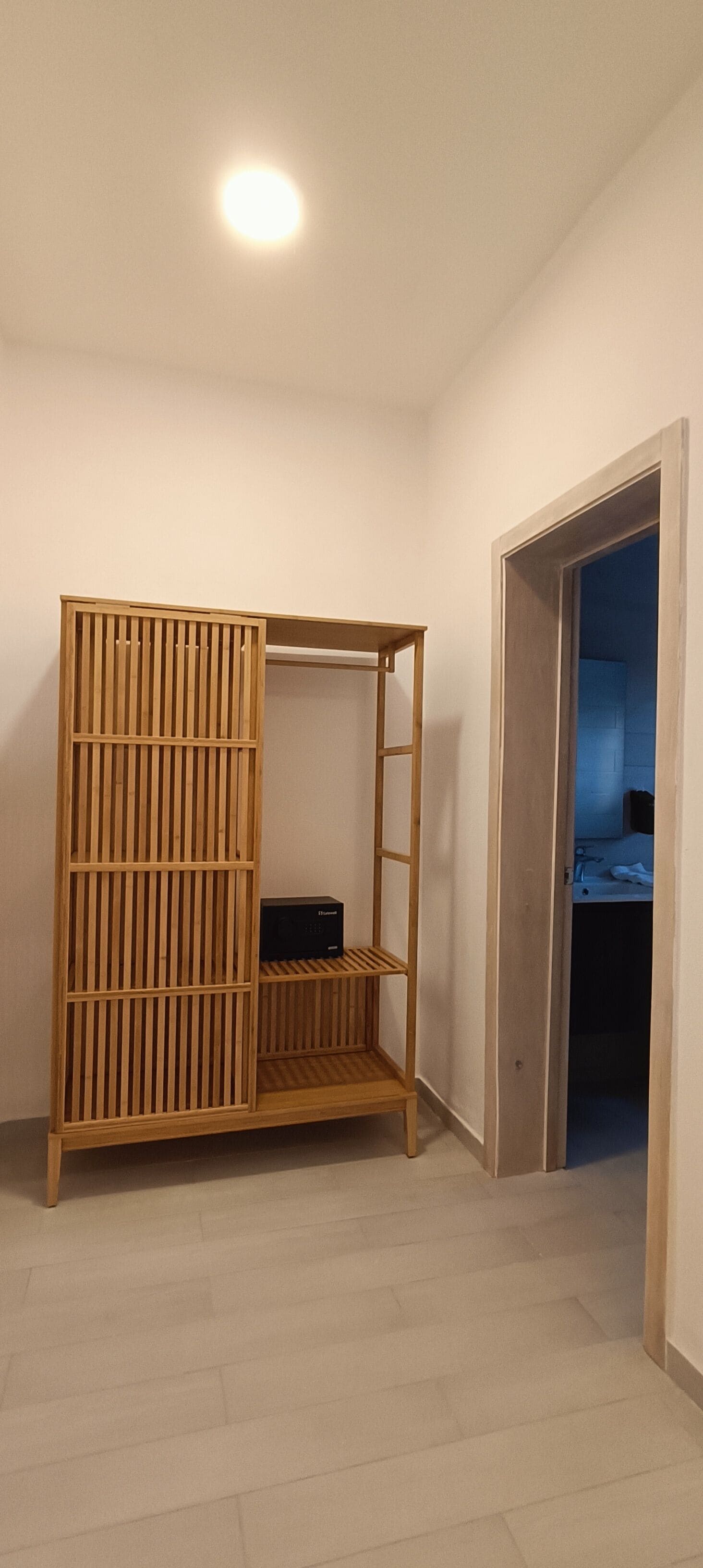 A room with a wooden wardrobe, a small table, and a door leading to a bathroom.
