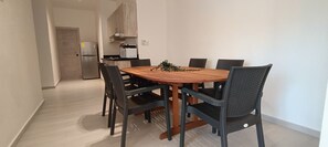 Un comedor moderno con una mesa de madera y sillas negras, una cocina al fondo y una puerta que conduce a otra habitación.