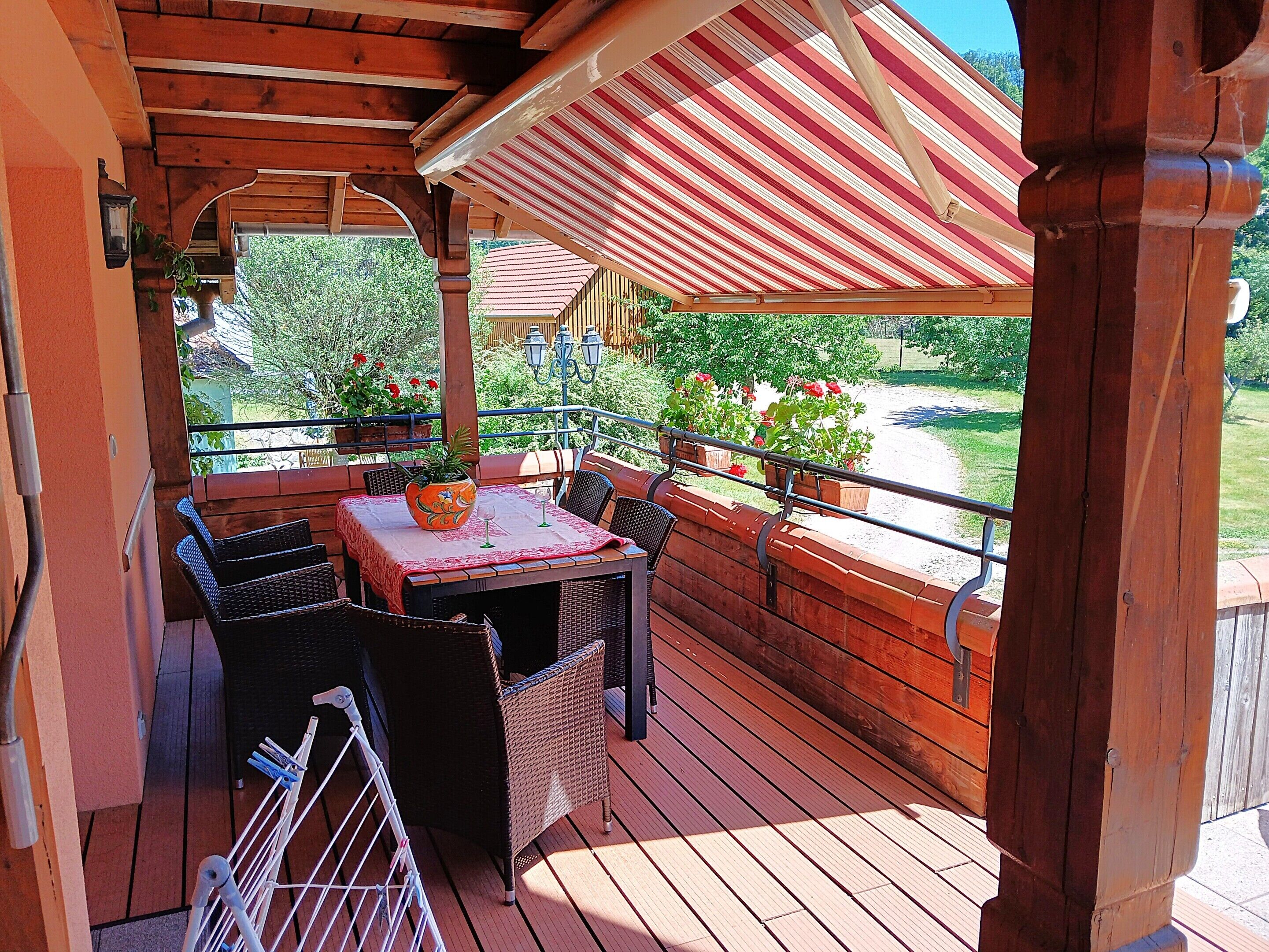 A wooden deck with a table and chairs, a railing, and potted plants.