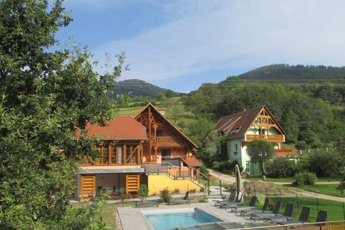 A hotel with a swimming pool, wooden architecture, and a view of hills.