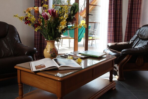 A wooden coffee table with an open book, a vase of flowers, and a leather chair.