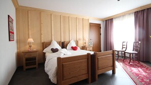 Ein Bett mit Kissen, ein Nachttisch, ein Sessel und ein roter Teppich in einem Raum mit Holzwänden und einer Tür.