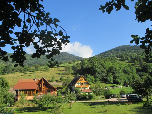 A rural setting with two traditional wooden houses surrounded by lush greenery and hills.