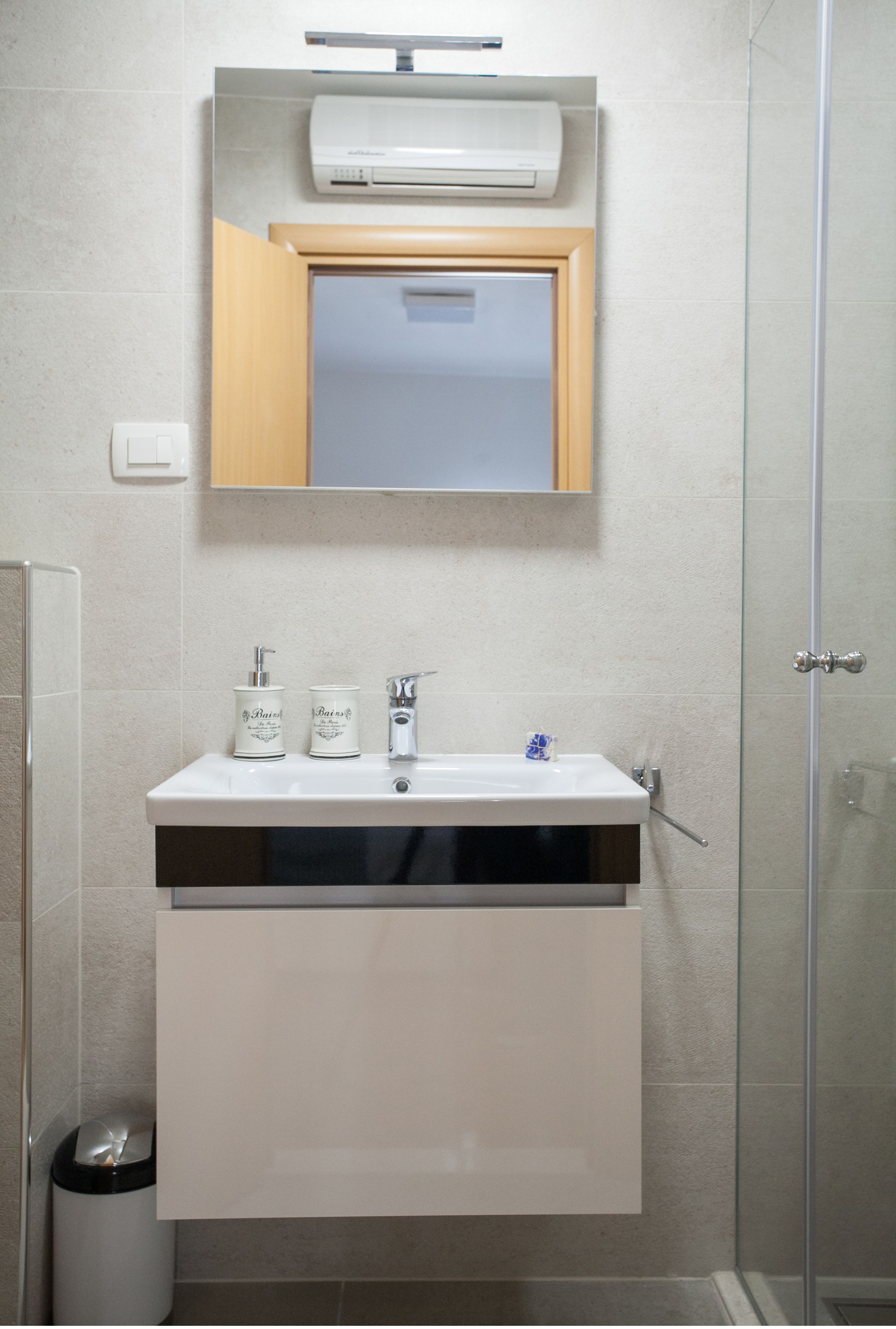 A bathroom with a white sink, two soap dispensers, a mirror, and a glass shower enclosure.