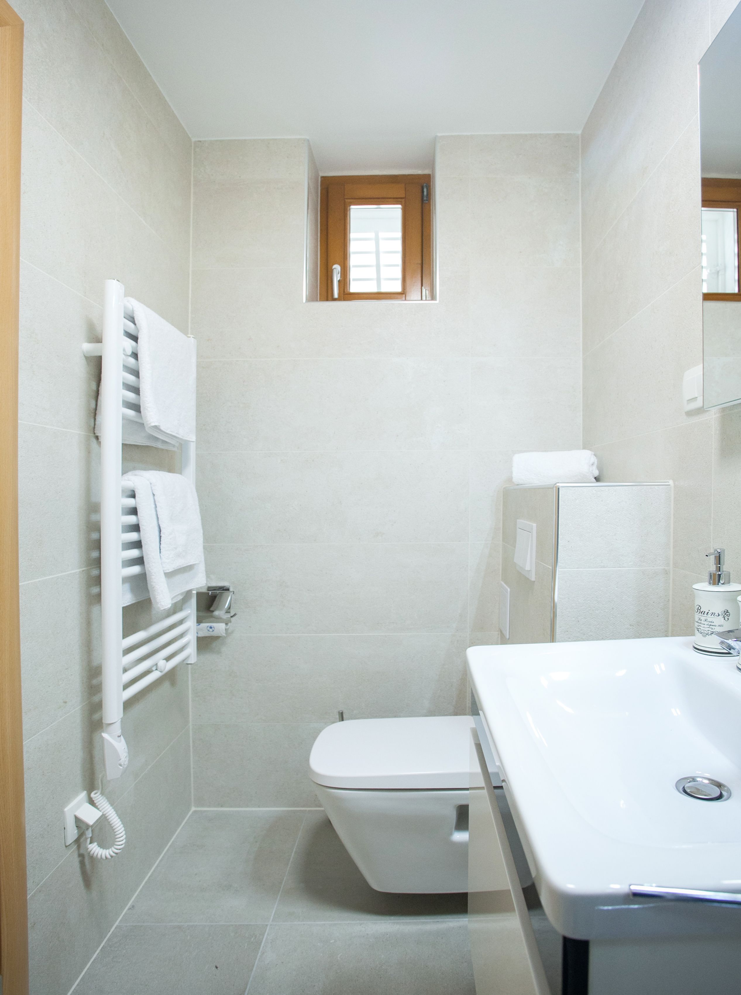A bathroom with a toilet, a sink, a towel rack, and a small window.