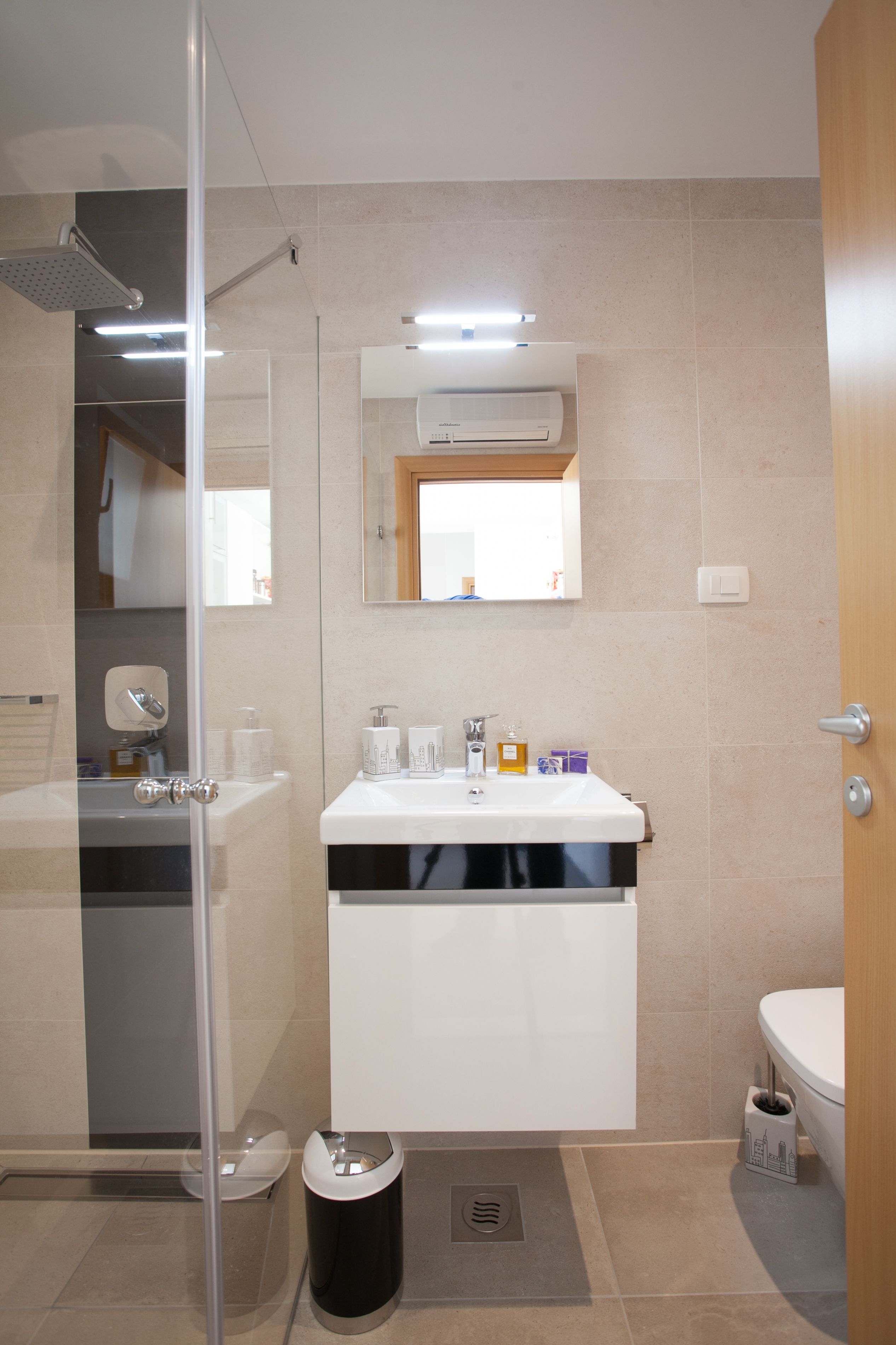 A modern bathroom with a glass shower enclosure, a white sink with a black base, and a toilet.