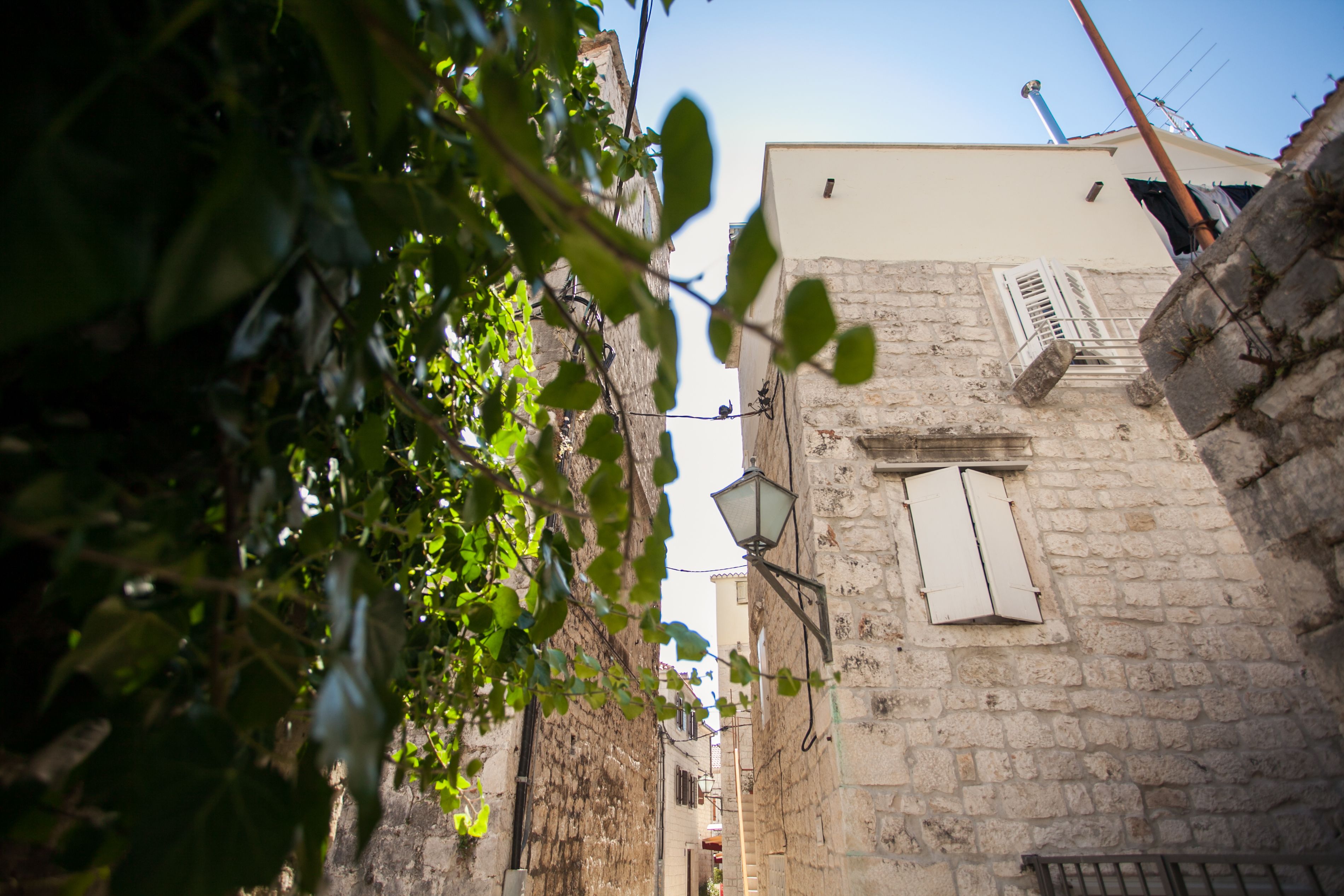 A narrow street with stone buildings, a visible window with shutters, and a street lamp.