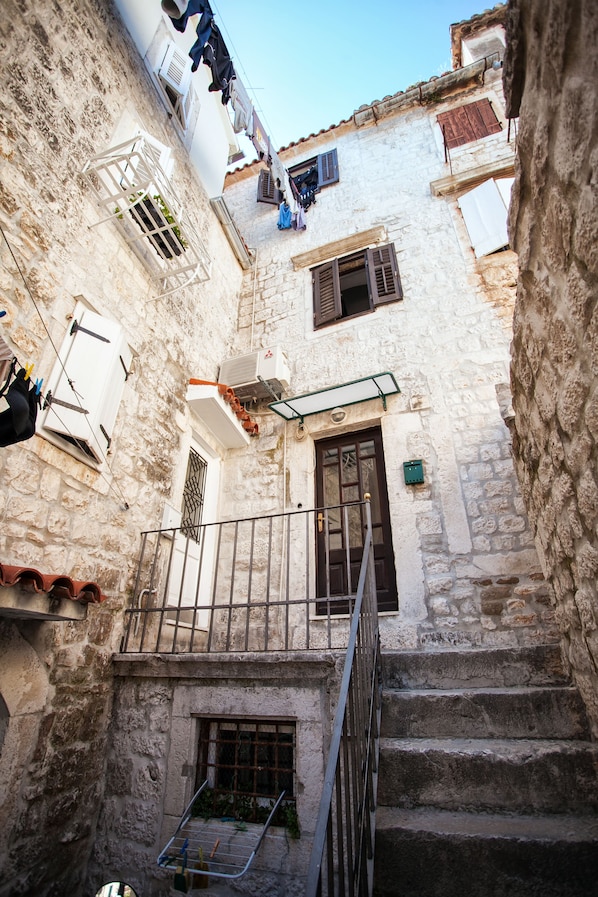A narrow street with a stone building, a wooden door, and a metal staircase. - Apartment heart of Trogir (Trogir)
