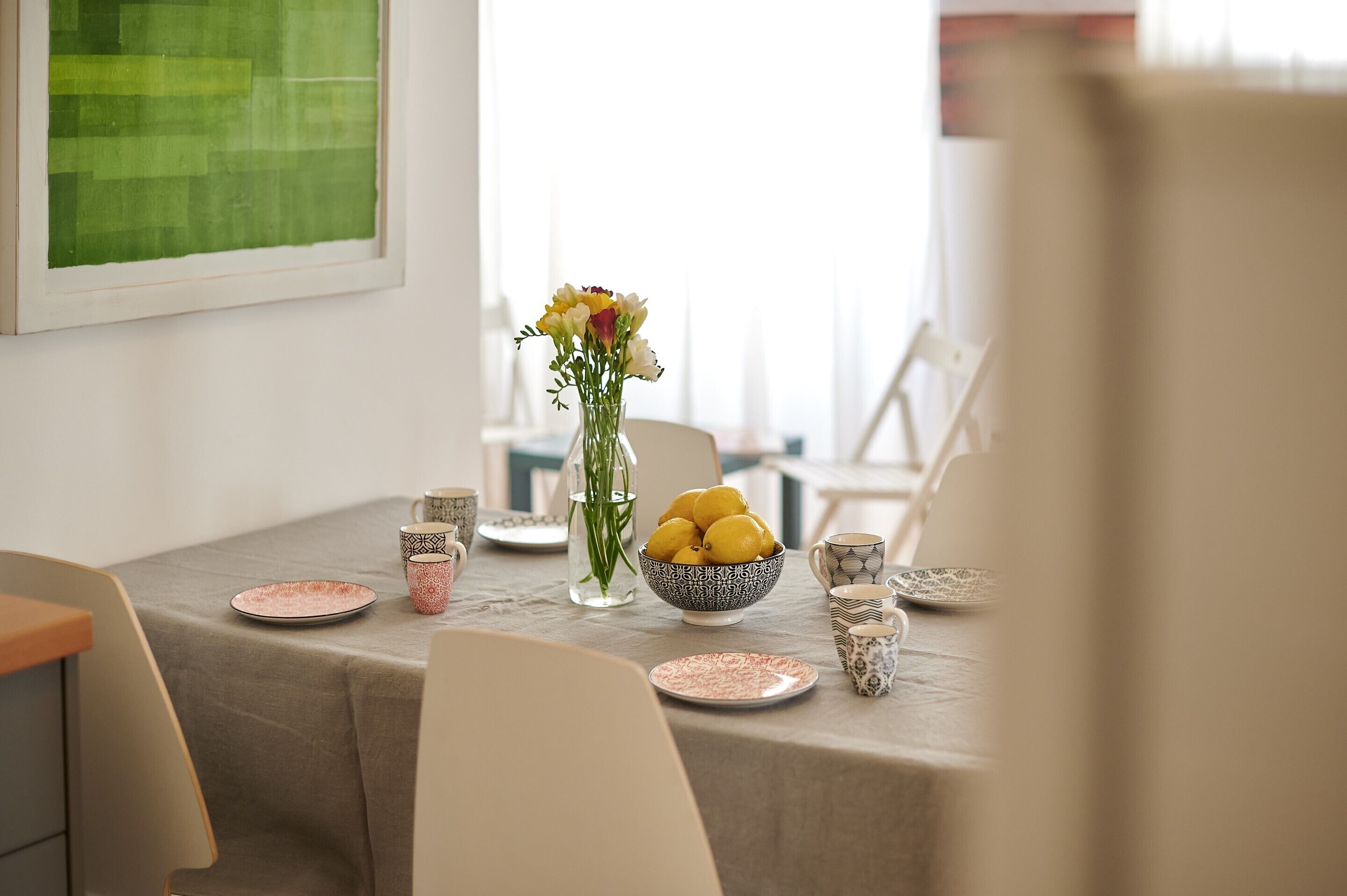 Une table à manger dressée avec des assiettes, un saladier rempli de citrons, un vase de fleurs et des tasses à motifs.