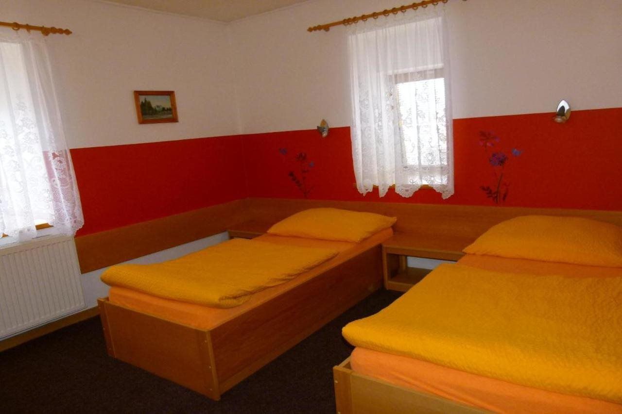 Una habitación con dos camas individuales, cortinas blancas, una pared roja y un cuadro pequeño en la pared.